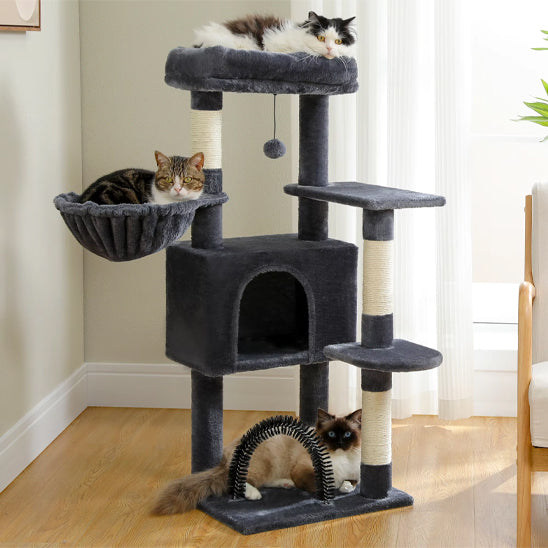 Arbre a chat bois avec trois niveaux gris foncé et trois chats, un sur le haut et un dans le hamac et l'autre à cÎté de la brosse auto-nettoyeur.