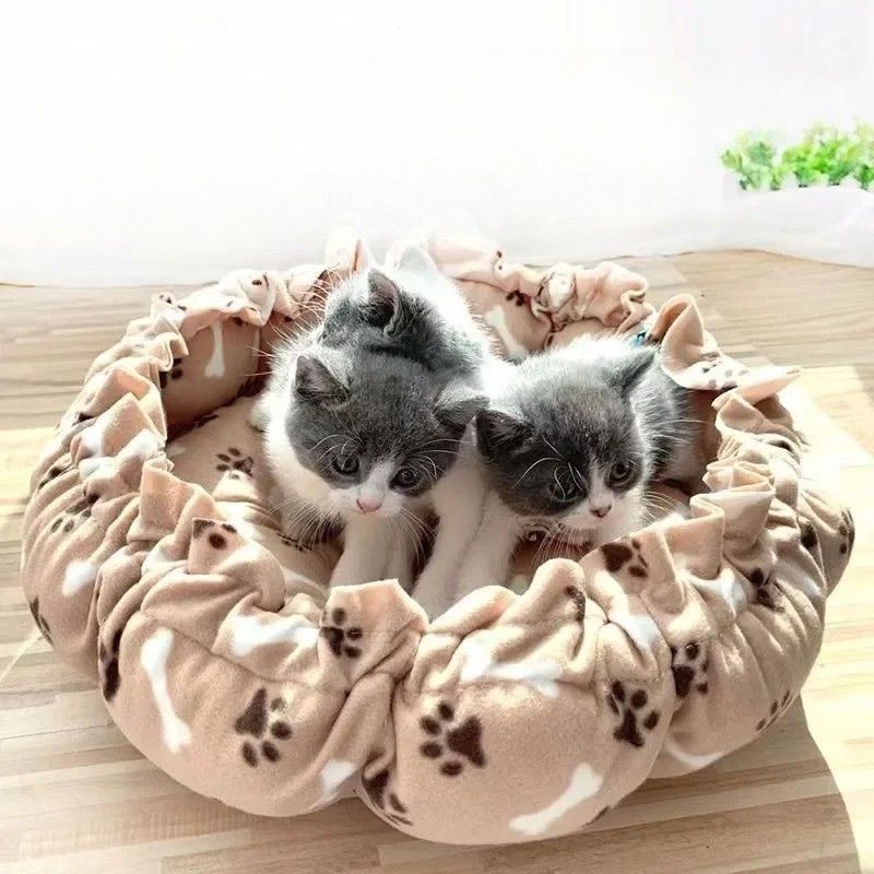 Un coussin chat en forme de nid avec un serrage tout le tour beige avec des motifs de pattes marron et os blancs.
