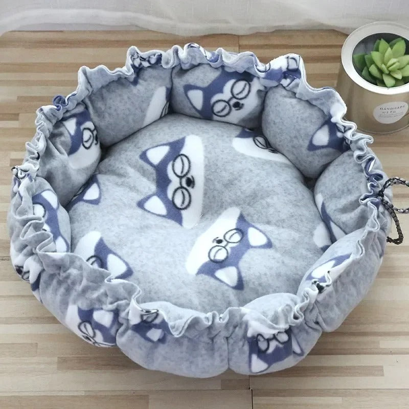 Un coussin chat en forme de nid avec un serrage tout le tour gris avec des motifs de visages de chats bleu et blanc.