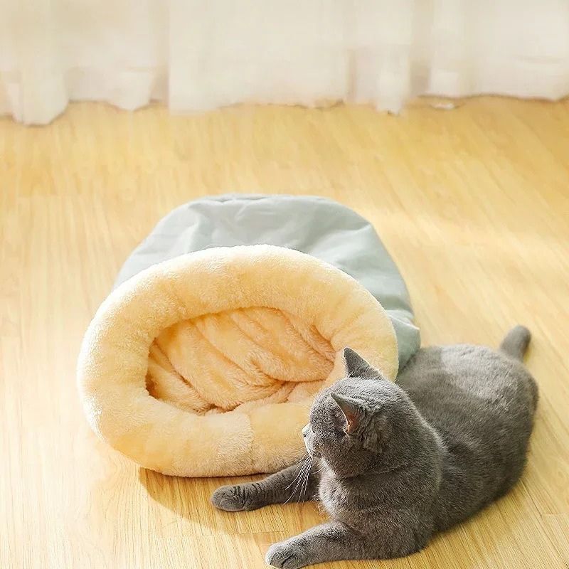 Coussin chat en forme de sac de couchage gris avec un chat allongé à cÎté de ce coussin.
