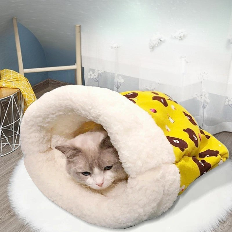 Coussin pour chat en forme de sac de couchage jaune avec des motifs dessus et un chat blanc allongé dedans.
