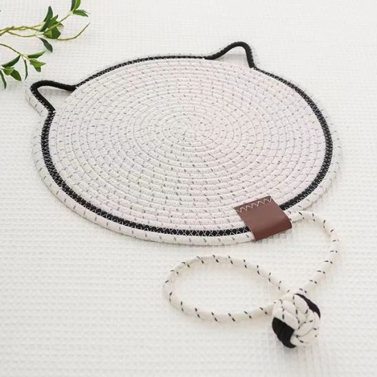 Un griffoir à chat en forme de tapis rond blanc avec un trait noir et des oreilles de chats tout le tour et une balle intégrée en corde de coton.
