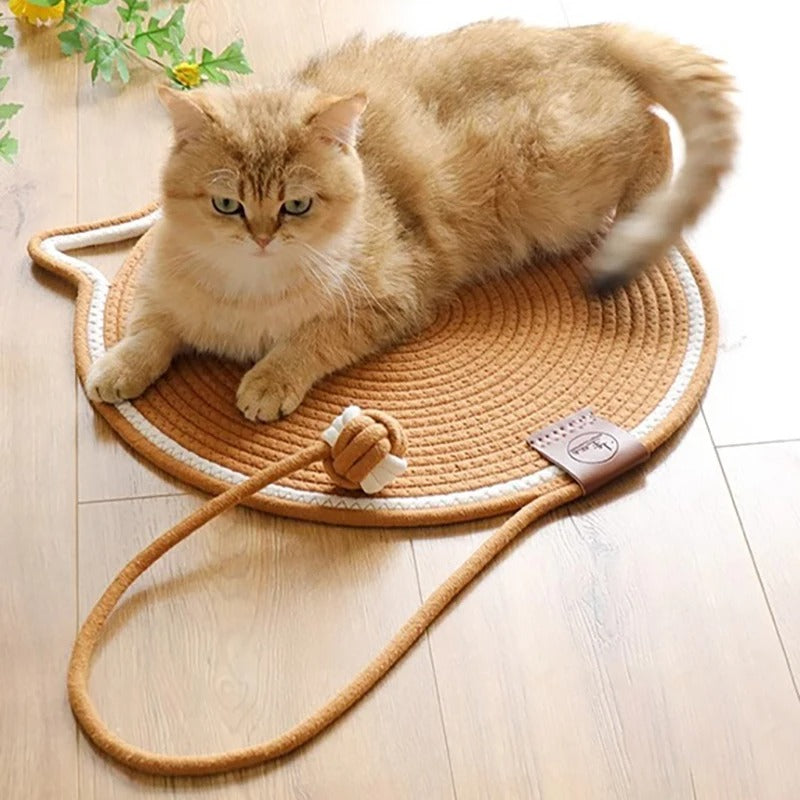 Un chat roux allongé sur un griffoir à chat en forme de tapis rond marron avec un trait blanc tout le tour et une balle intégrée en corde de coton.