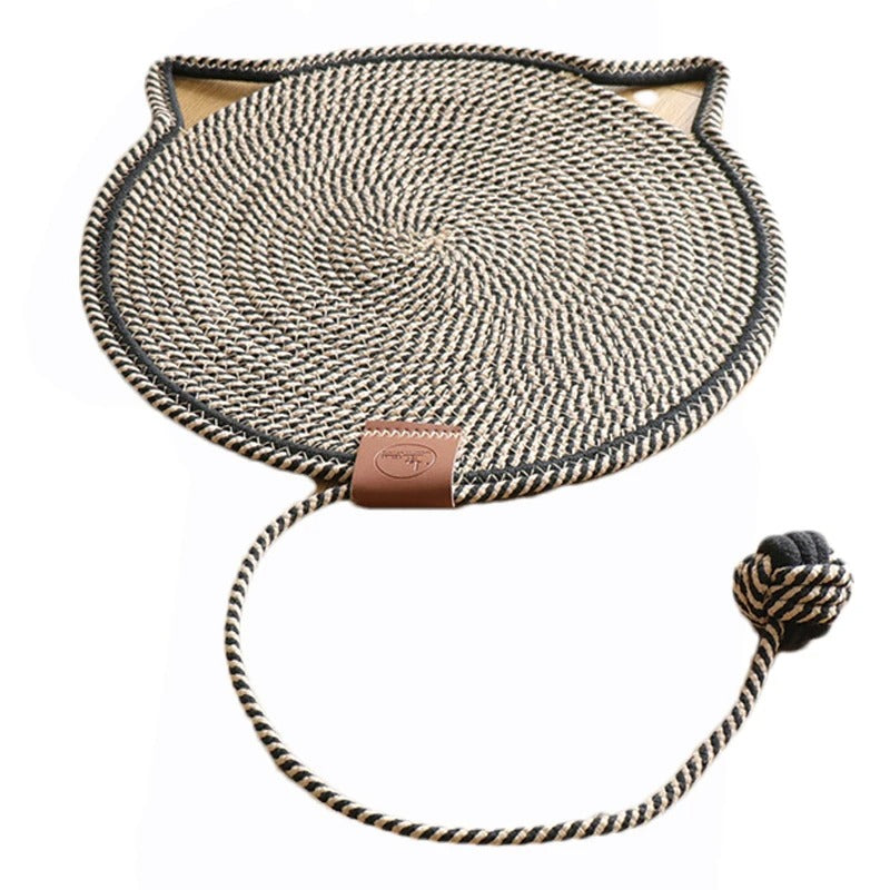 Un griffoir à chat en forme de tapis rond beige et noir avec un trait noir et des oreilles de chat tout le tour et une balle intégrée en corde de coton.