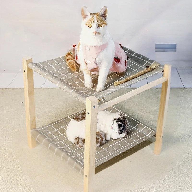 Un hamac à chat en forme de lit superposé en deux étages en bois et des sièges en toile à carreaux gris et blanc avec deux chats blancs, une chatte avec une robe rose à motifs de fraise assise en haut et l'autre chaton qui dort en bas.