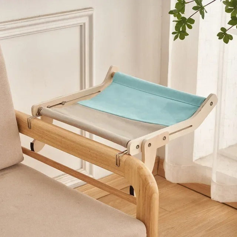 Un hamac chat moitié gris moitié bleu accroché à un accoudoir d'un fauteuil de salon en bois.