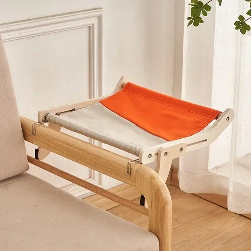 Un hamac chat moitié beige moitié orange accroché à un accoudoir d'un fauteuil de salon en bois.