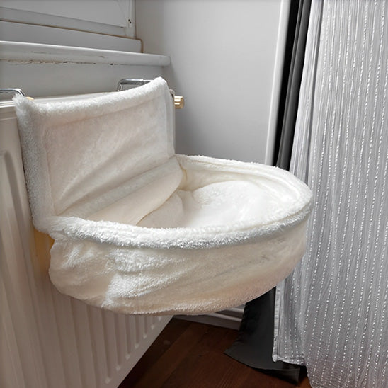 Hamac radiateur chat blanc placé sur un radiateur dans une chambre.