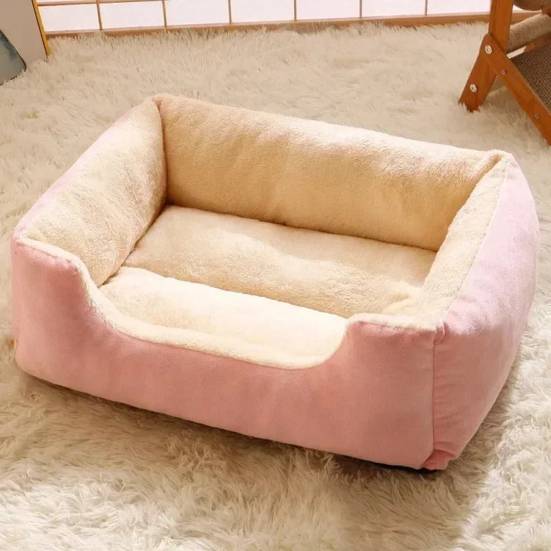 Lit pour chat en forme de canapé rectangulaire rose et blanc à l'intérieur avec un chat marron allongé dessus.