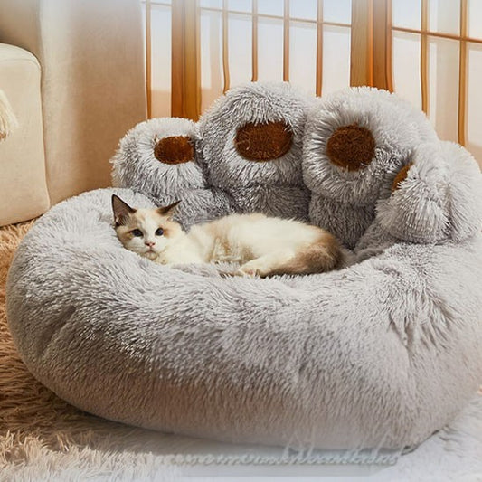Lit pour chat en forme de patte d'ours en peluche café dégradé et les pattes en marron avec un chat beige allongé dessus.
