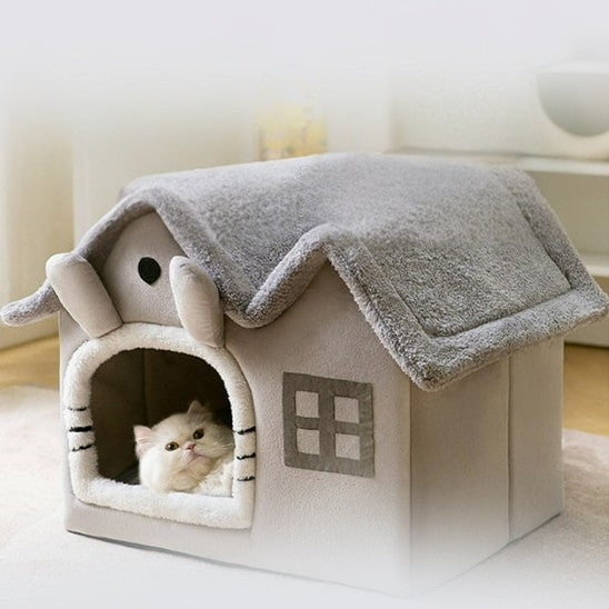 Maison pour chat grise spacieuse avec deux longues oreilles avec un chat blanc allongé dedans et qui regarde.