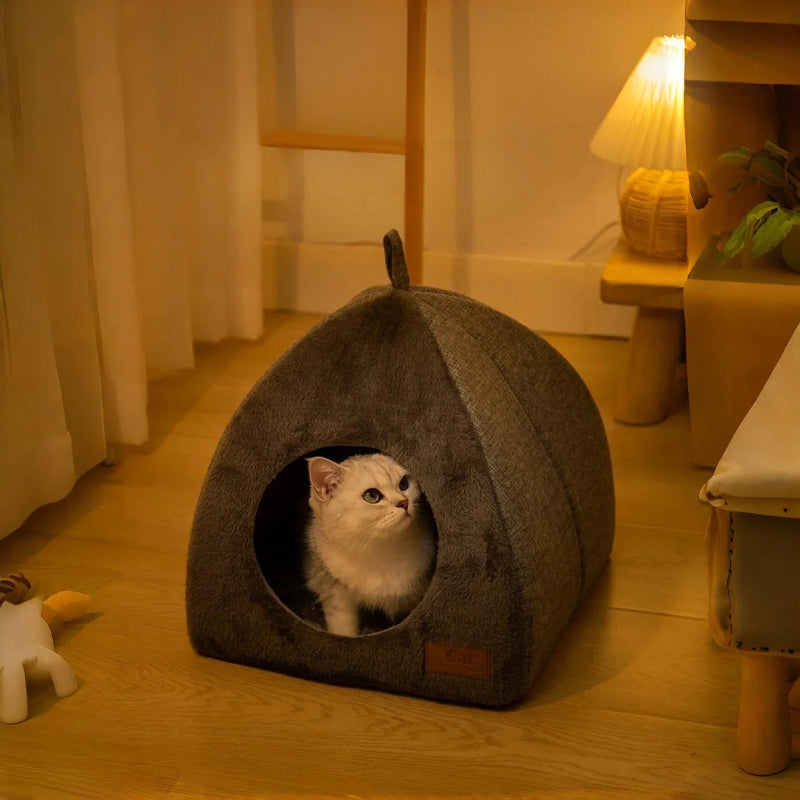 Maison pour chat en forme de petite niche grise avec un chat blanc assis dedans.