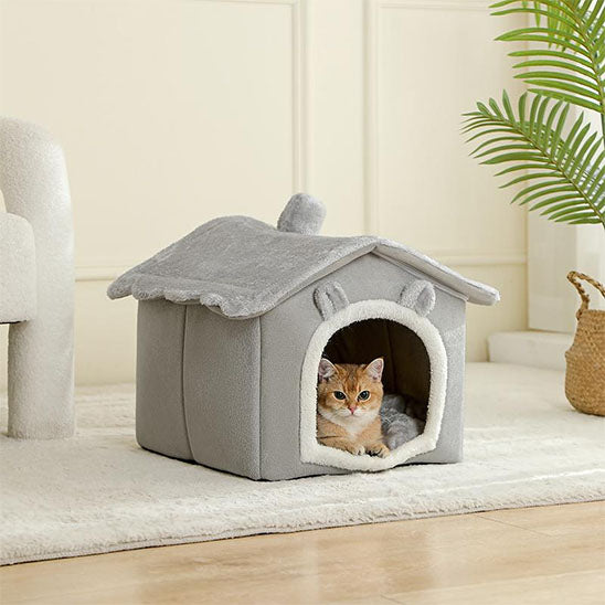 Niche à chat grise en forme de maison avec deux oreilles de chat et un chat roux allongé dedans.