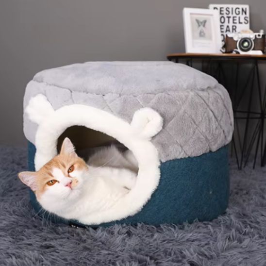niche à chat ronde en forme de pouf moitié en hat grise et en bas bleu-vert avec un chat roux allongé dedans.