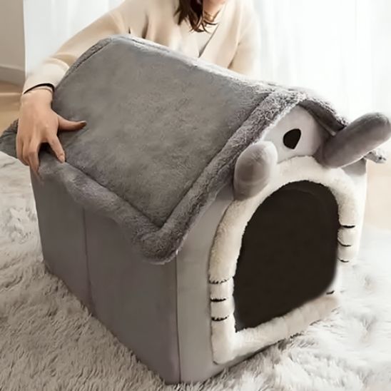 Niche chat en forme de maison grise avec un coussin intégré dedans et en et une femme assise derriÚre cette niche.