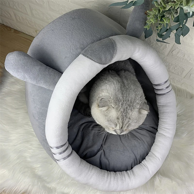 niche pour chat grise en forme de chinchilla avec des oreilles et une balle suspendue en haut et un chat gris assis dedans.