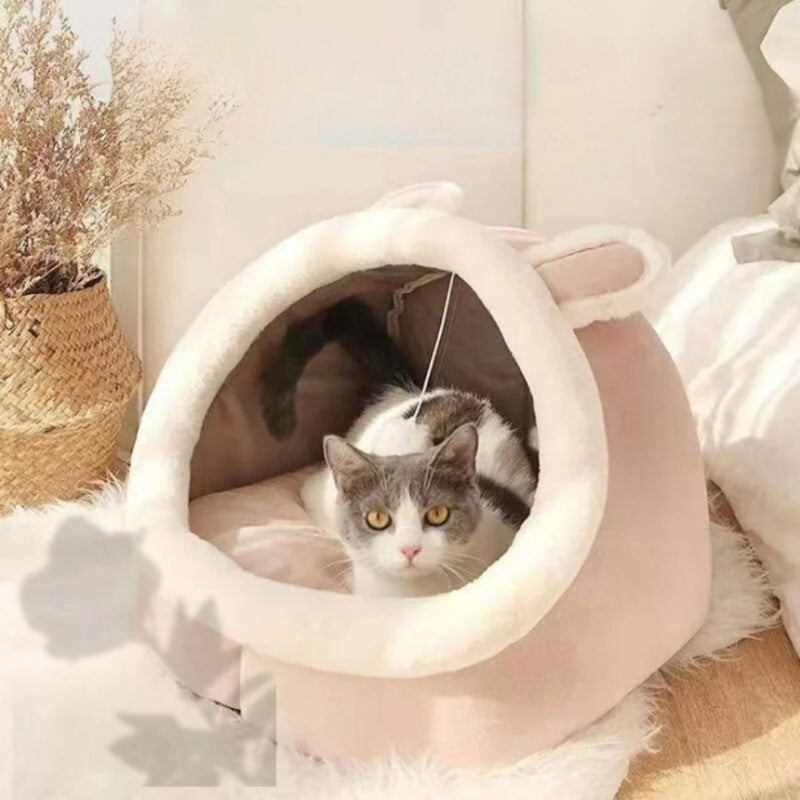 Niche pour chat rose en forme de lapin avec des oreilles et un chat gris et blanc assis dedans.