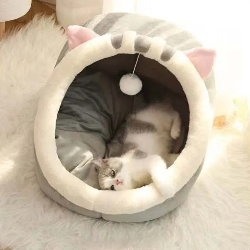 Niche pour chat grise en forme de chaton avec des oreilles et une balle suspendue en haut et un chat allongé dedans.