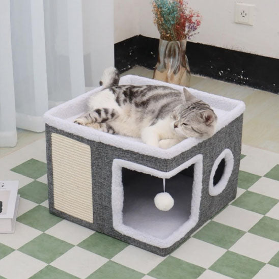 Niche pour chaton en forme de cube grise et blanche avec deux ouvertures, une zone de grattage et boule suspendue avec un chat gris endormi sur la zone en haut.