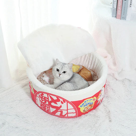 Panier chat en forme de pot de nouilles rouge avec motifs et un chaton allongé dedans.