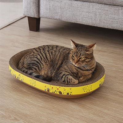 Panier pour chat ovale avec bande jaune avec motifs et un chat tigré allongé dessus.