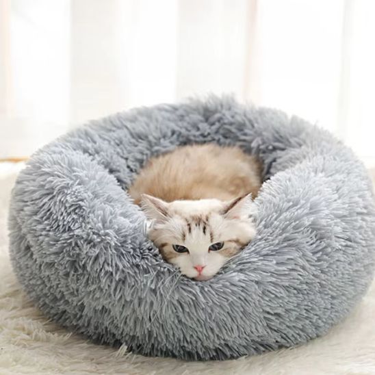 Un coussin à chat rond en peluche, rond et profond, gris avec un chaton beige allongé dedans.