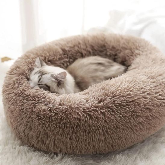 Un coussin à chat rond en peluche, rond et profond marron avec un chaton beige qui dort dedans.