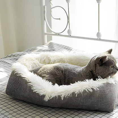 Coussin chat pliable gris avec peluche blanche plié avec un chat gris assis dedans sur un lit dans une chambre.