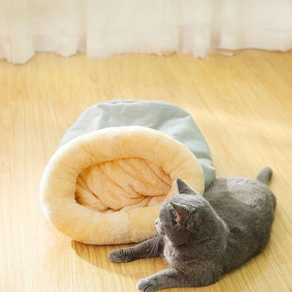 Coussin chat en forme de sac de couchage gris avec un chat allongé à côté de ce coussin.