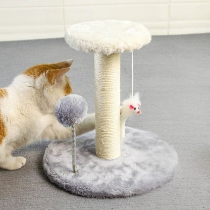 Un chat blanc et marron en train de jouer avec un grattoir chat en forme d'un poteau en sisal avec deux bases, une grande grise et l'autre en haut petite blanche avec deux peluches en forme de souri et boule suspendu