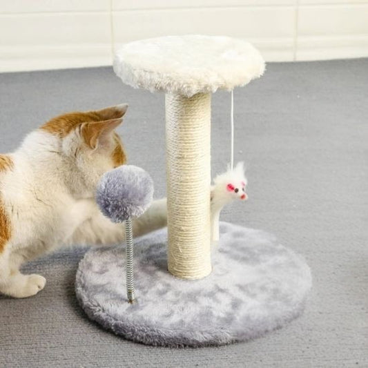 Un chat blanc et marron en train de jouer avec un grattoir chat en forme d'un poteau en sisal avec deux bases, une grande grise et l'autre en haut petite blanche avec deux peluches en forme de souri et boule suspendu