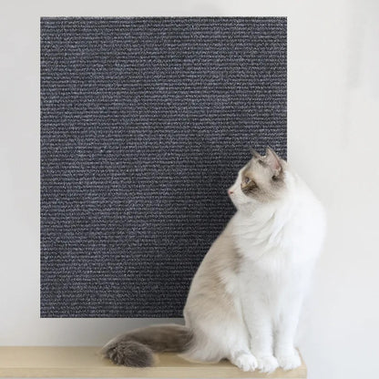 Un chat blanc assis à côté d'Un griffoir à chat gris foncé collé sur un mur.