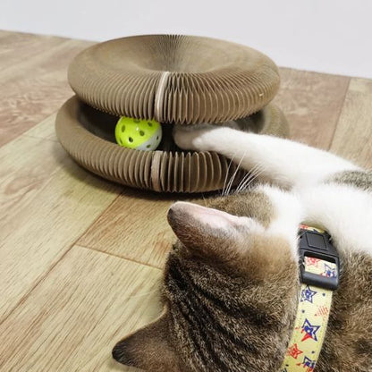 Un griffoir chat carton marron rond avec un espace entre le haut et le bas et une balle qui roule dans cet espace avec un chat marron qui joue avec.