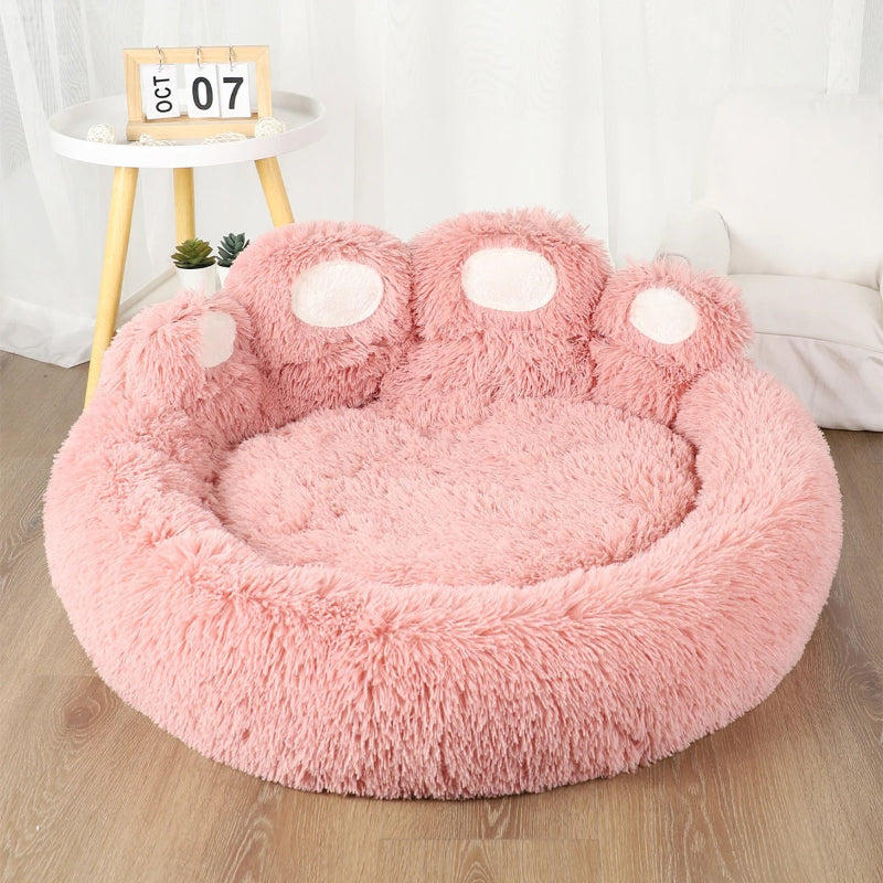 Lit pour chat en forme de patte d'ours en peluche rose et les pattes en blanc.