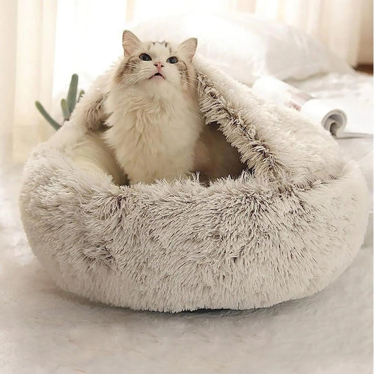 Lit pour chat en forme de petite grotte semi-fermée en peluche grise avec un chat blanc assis dedans.