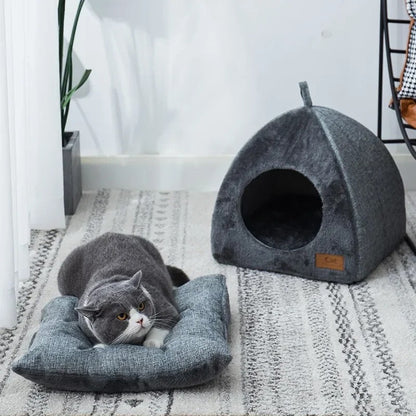 Maison pour chat en forme de petite niche grise avec un chat allongé à côté sur le coussin qui vient avec cette maison.