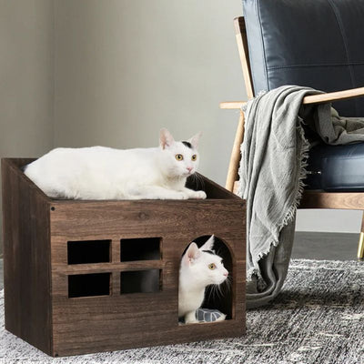 Niche à chat en forme de meuble de salon en bois avec un chat blanc allongé au-dessus et un autre à l'intérieur sur le coussin en bas de la niche.