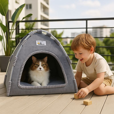 Niche à chat en forme de tente solide bleue placée sur le sol d'une terrasse de maison avec un chat assis dedans et un petit garçon assis à côté et en train de jouer avec le chat.