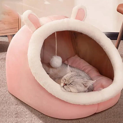 Niche chat forme d'oreilles de lapin rose avec un chat gris qui dort dedans.
