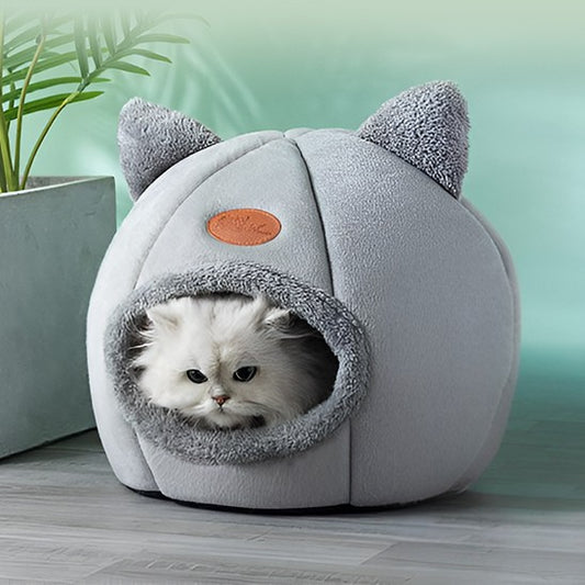 Niche pour chat ronde grise avec deux oreilles dessus et un chat blanc assis dedans.