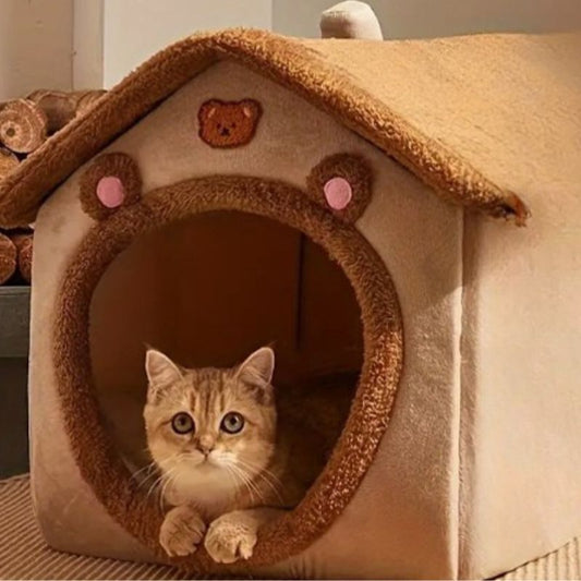 Niche pour chat en forme de maison marron avec un chat roux assis dedans et qui regarde.