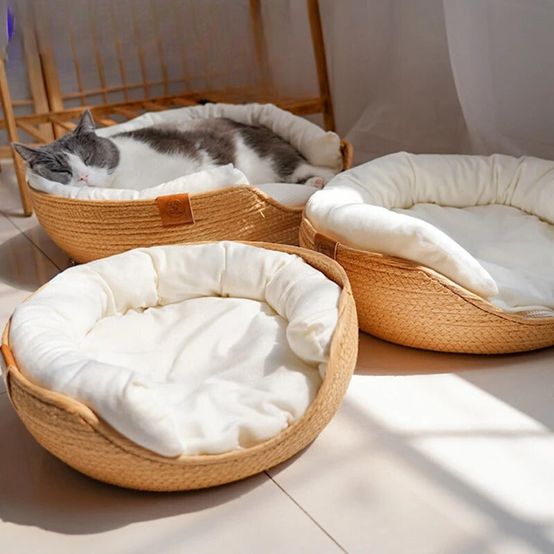 Panier osier chat beige avec un coussin blanc à l'intérieur avec un chat gris et blanc endormis dedans.