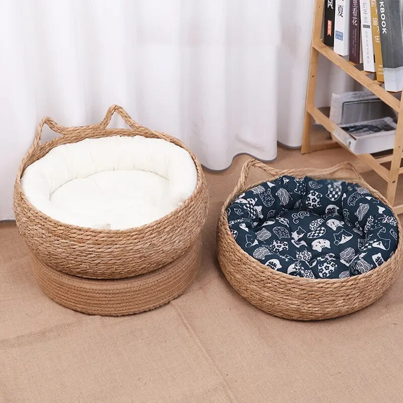 Panier osier chat beige avec un coussin blanc à l'intérieur et l'autre avec un coussin bleu avec des motifs blancs et deux formes d'oreilles de chat et un chat gris et blanc qui dort dedans.