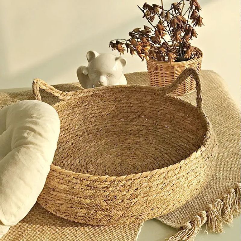 Panier osier chat beige avec deux formes d'oreilles de chat et un coussin blanc sur le côté de ce panier.